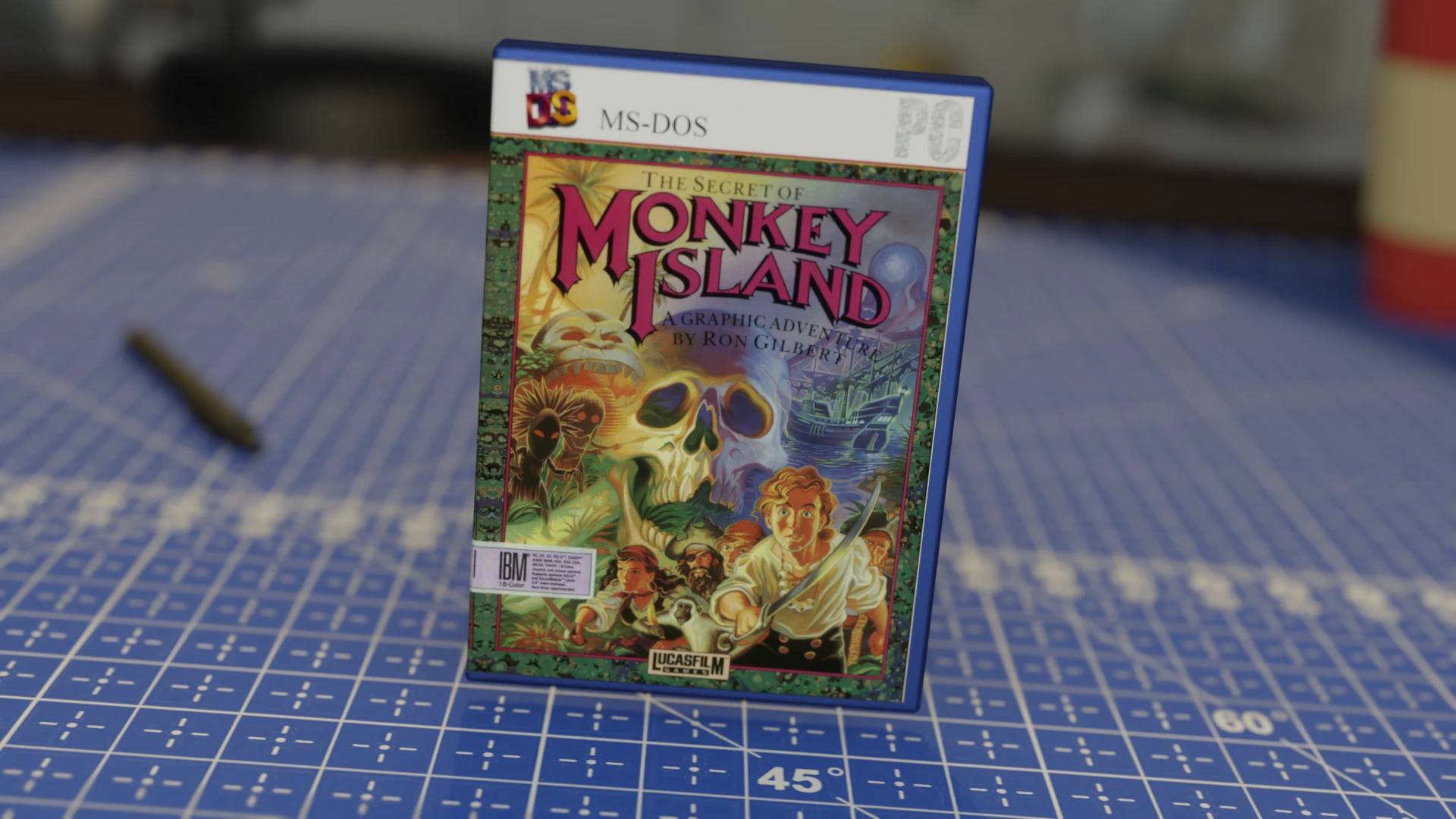Caja del videojuego The Secret of Monkey Island para MS-DOS en una funda de plástico azul, colocada sobre una superficie azul cuadriculada con herramientas desenfocadas en el fondo.