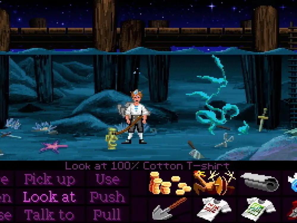 Guybrush Threepwood bajo el agua, atado a un ídolo de piedra, rodeado de objetos sumergidos y con una camiseta en su inventario.